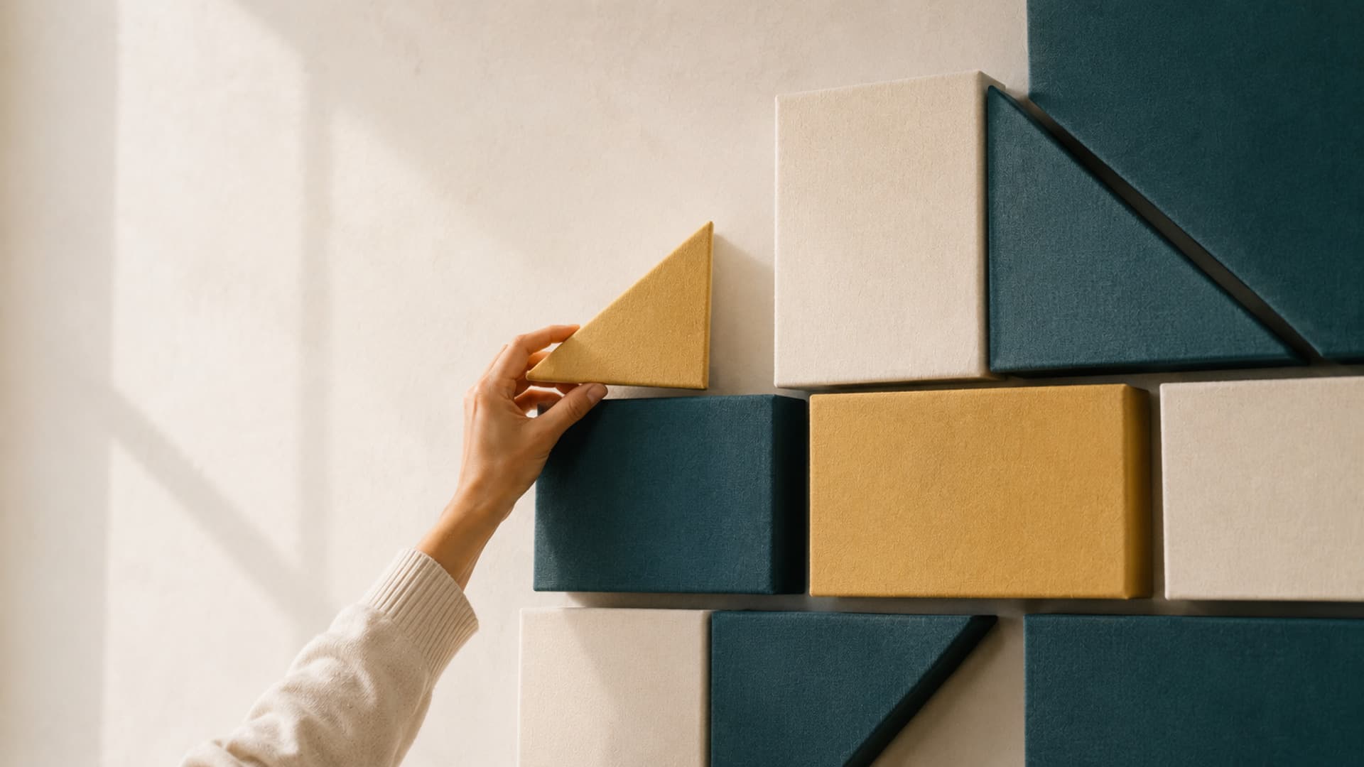 A hand placing a triangular block onto a stack in a sunlit, textured room
